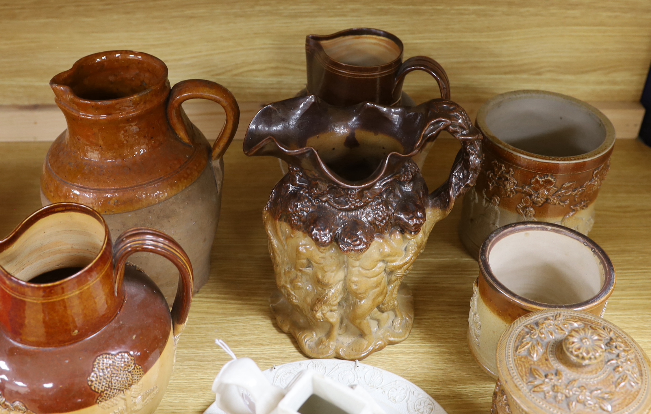 A Victorian stoneware jug, the sides moulded with bacchanalians, together with other earthenware jugs, a white salt glazed dish and 'house' teapot, the latter lacking lid, the largest 23cm high